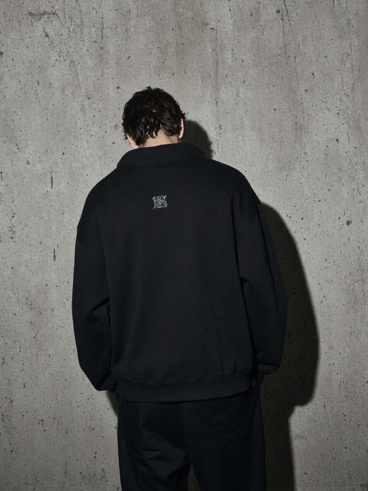 Model in a black embroidered sweatshirt against concrete